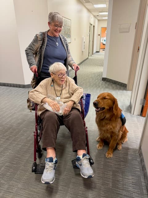 Rosco sitting beside a patient in a wheelchair in the office hallway